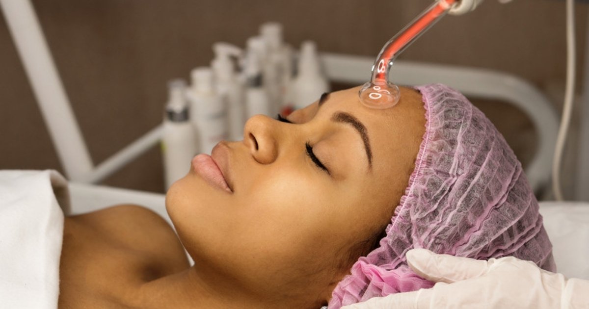 A relaxed client receiving a high frequency facial, with a glowing glass electrode on her forehead
