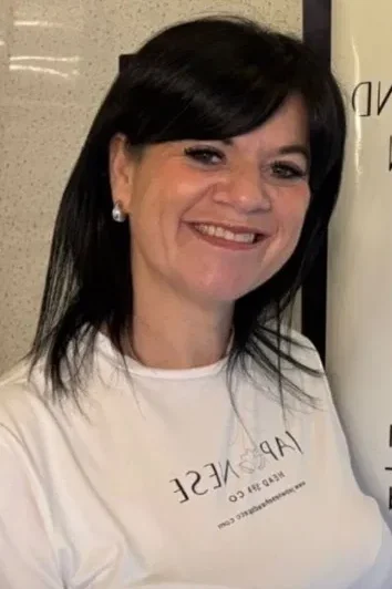 Jenn from Japanese Head Spa Training smiling, with dark shoulder-length hair, wearing a white Japanese Head Spa Co t-shirt