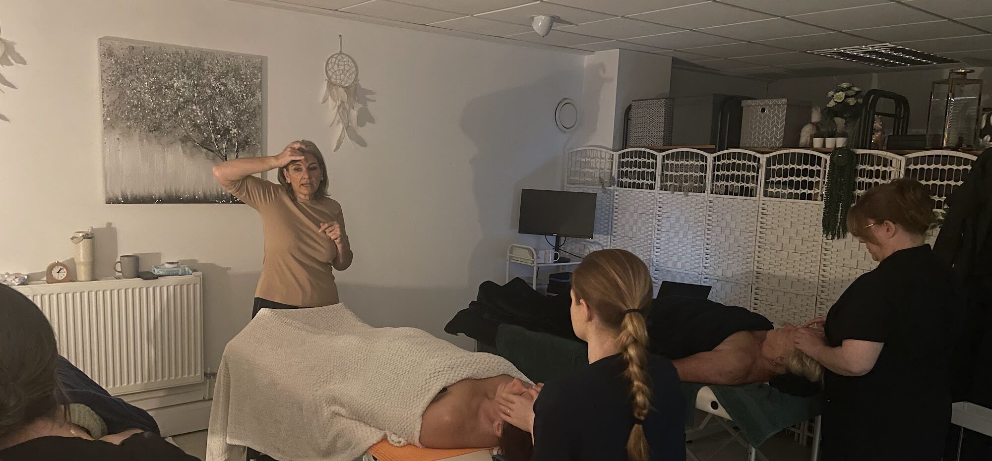A group of students practising massage on clients lying on treatment couches during a practical training day