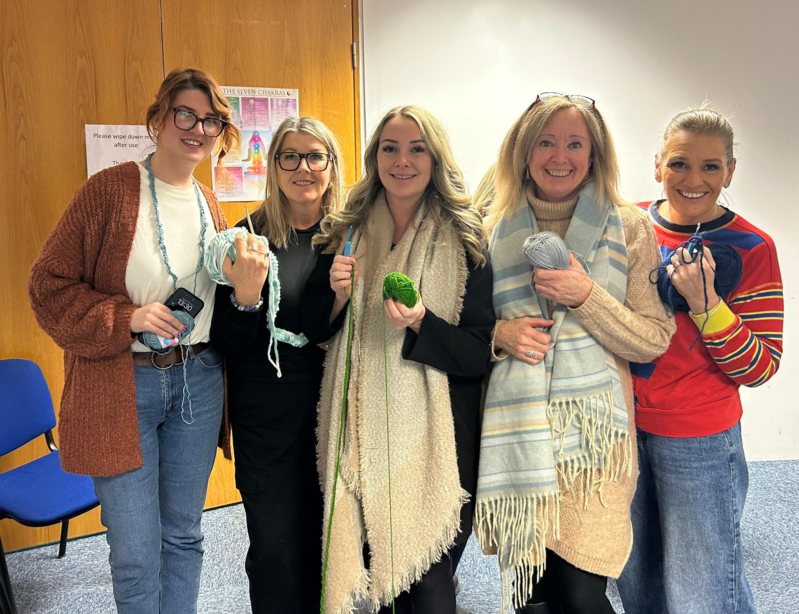 Five practitioners from Plymouth Wellbeing Centre smiling together, each holding a ball of wool for a crochet session: Taylor, Tracy, Lianne, Viv and Karen