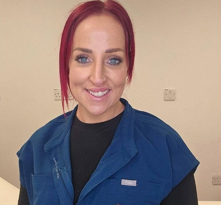 Sian, permanent makeup artist, smiling in her navy work tunic in a treatment room