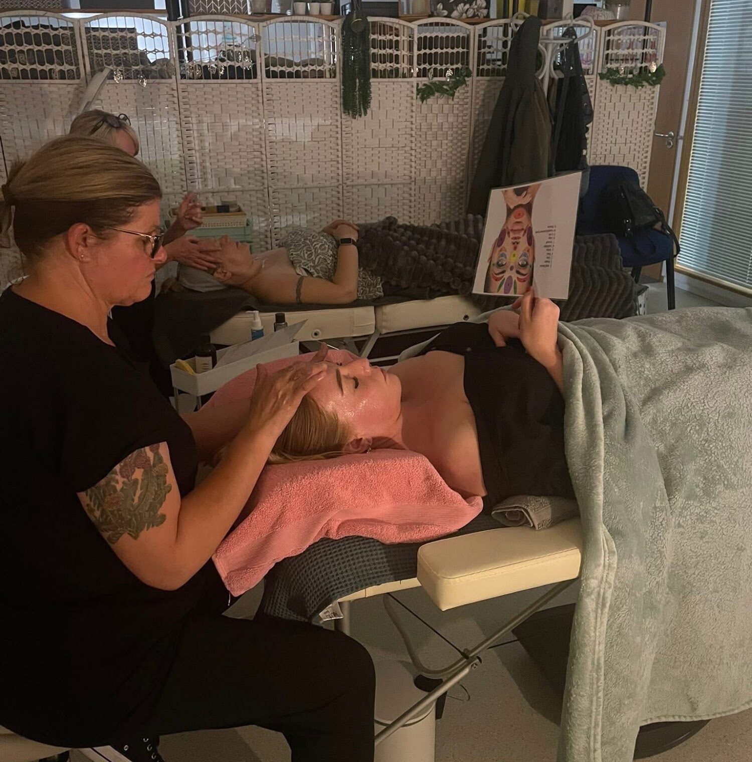 A student giving a facial treatment to a client lying on a couch during a training day