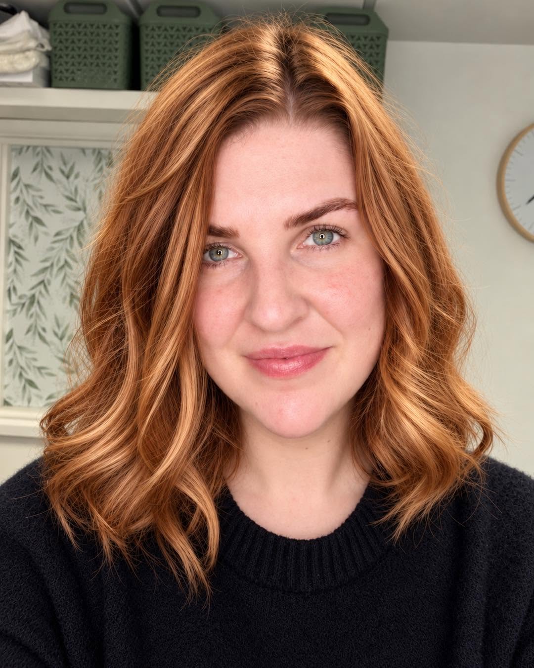 Taylor from Taylor Vaughan Aesthetics and Acupuncture, smiling, with wavy copper hair and a black jumper