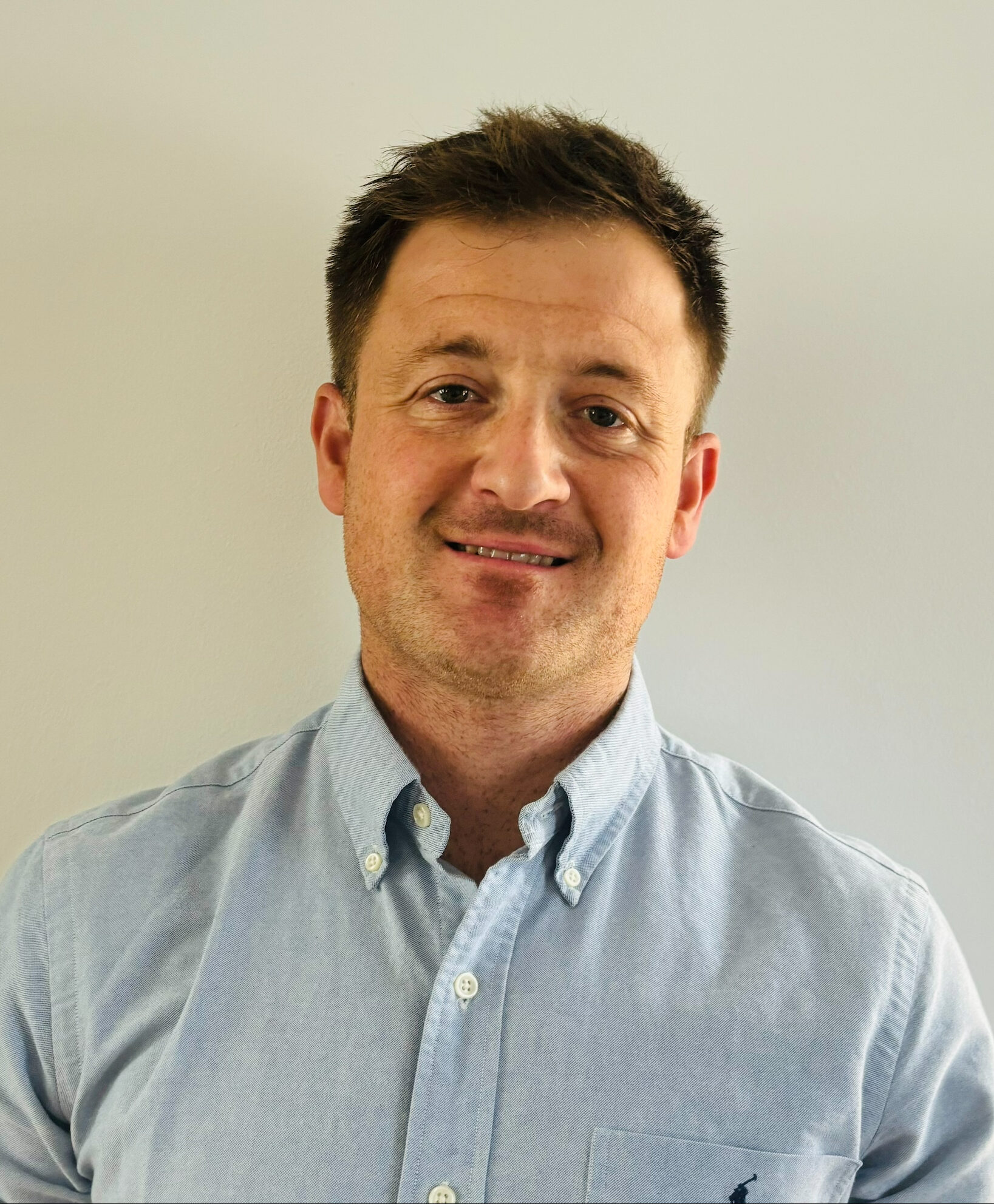 Tom Varcoe from Tom Varcoe Physiotherapy smiling, with short dark hair and a light blue shirt