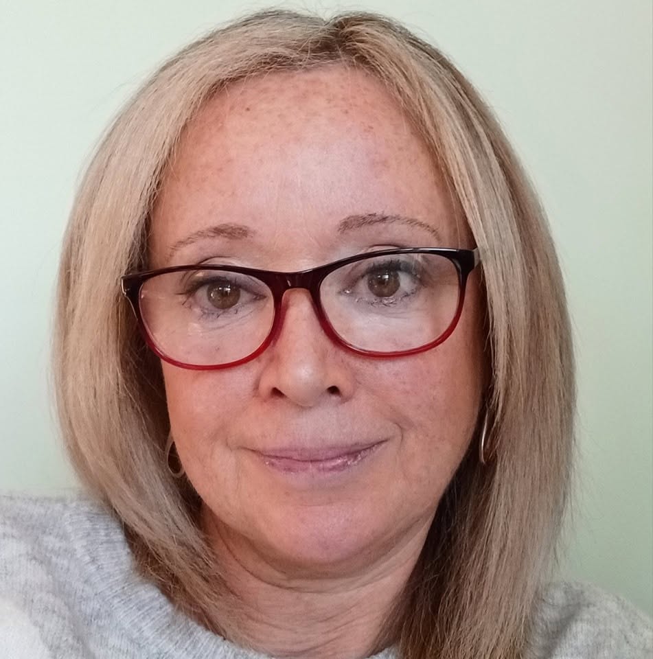 Viv from Invest in You with Vivienne smiling gently, wearing red-framed glasses and a soft grey jumper