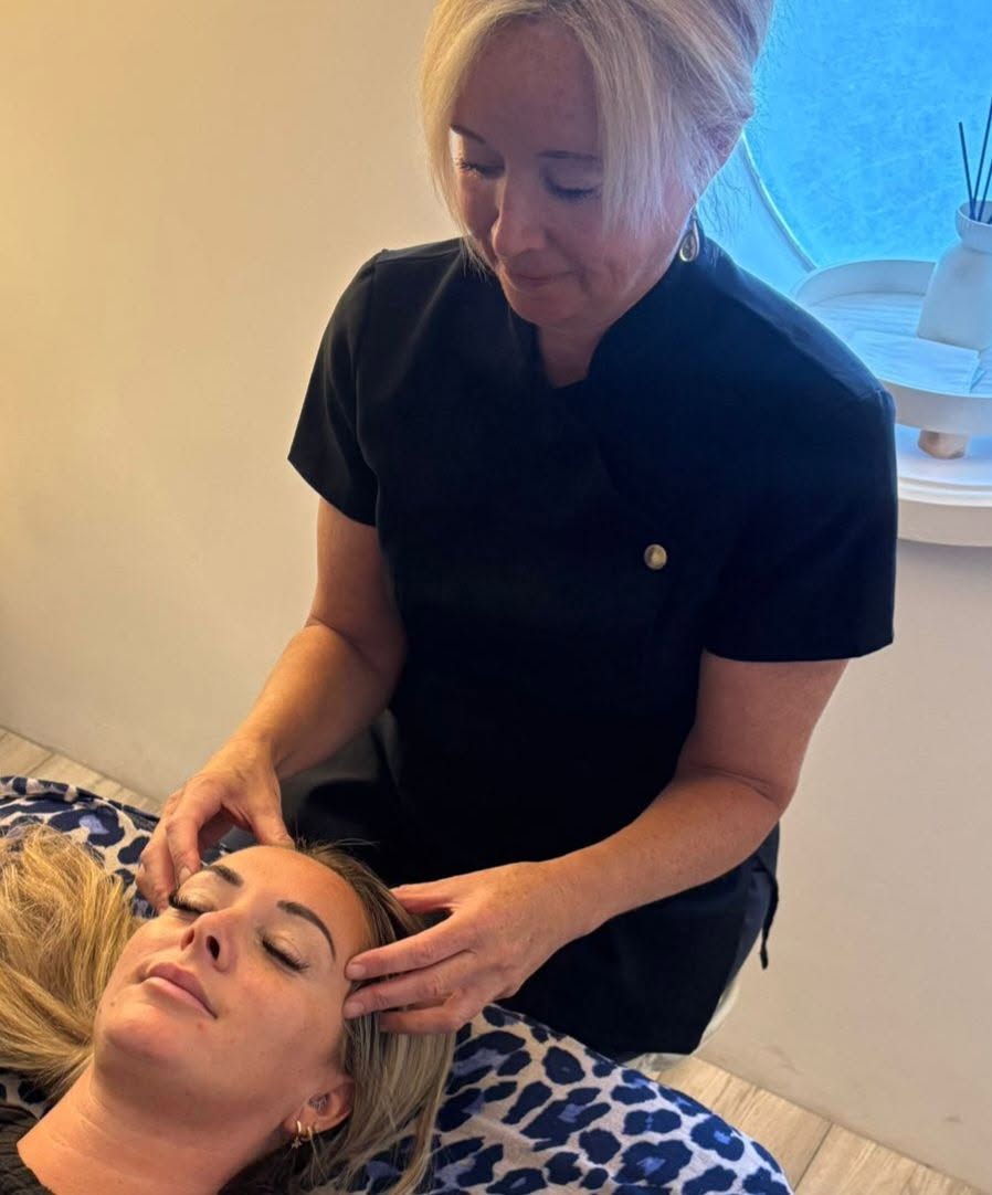 Viv giving a calming head treatment to a client lying on a couch in the bright treatment room with porthole windows