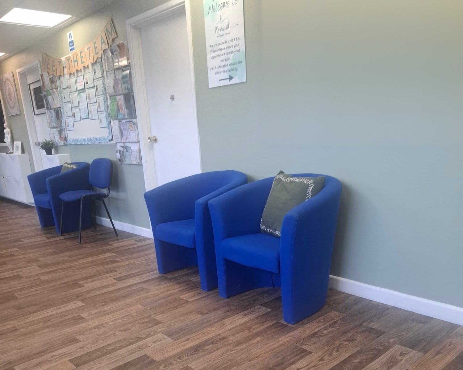 The welcome area with blue armchairs, a wood-effect floor, a welcome sign and a noticeboard