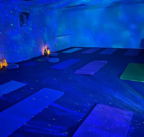 The community space set up for a yoga class, with mats laid out in rows, cushions, lanterns and starry blue lighting across the walls
